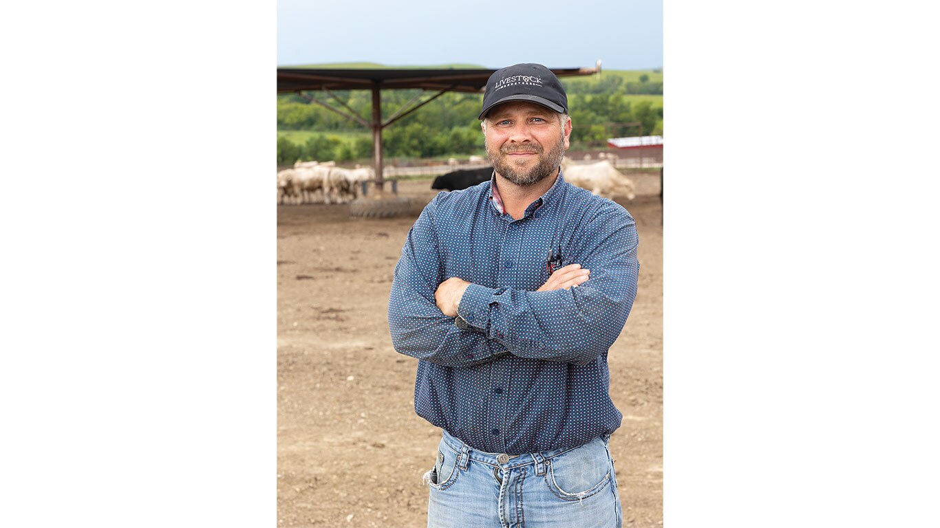 Person in a blue shirt and black ball cap standing in a pen with cows in the background.