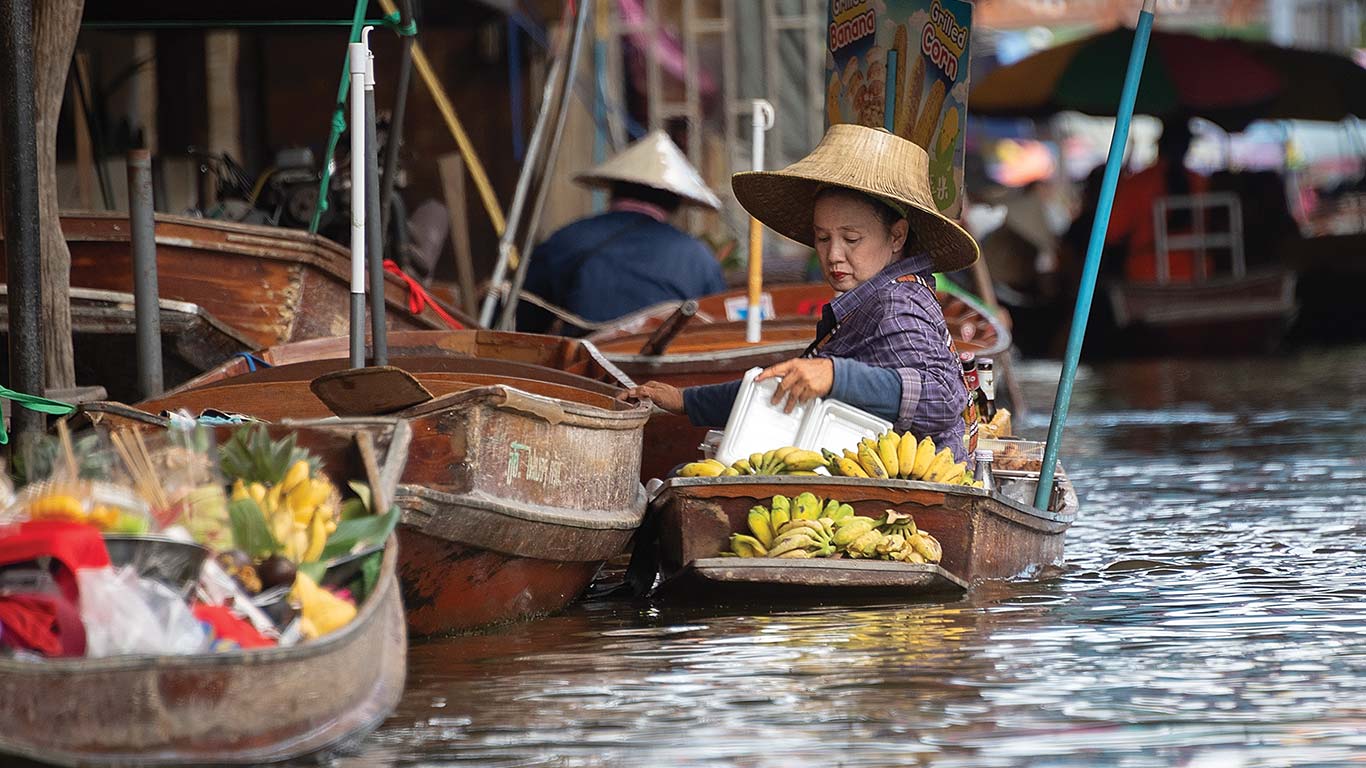 Wooden boats on a canal selling bananas and produce at a floating market.