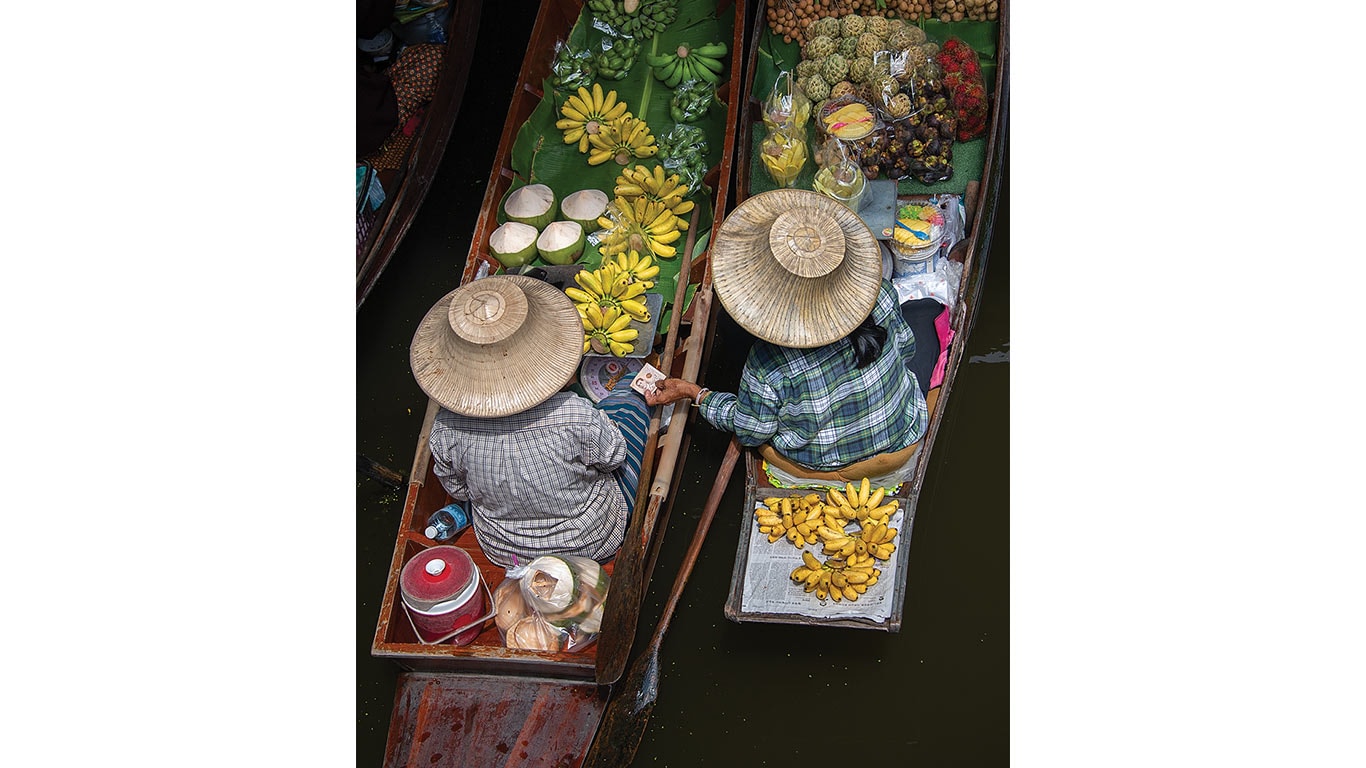 Two wooden boats at a floating market filled with bananas, coconuts, and assorted fruits.