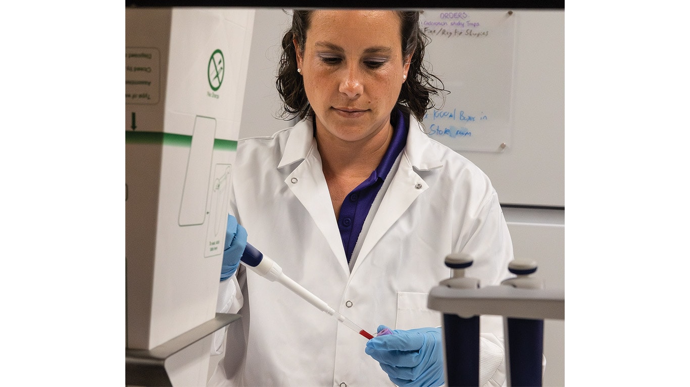 Person in a lab coat using a pipette to transfer liquid into a small test tube.