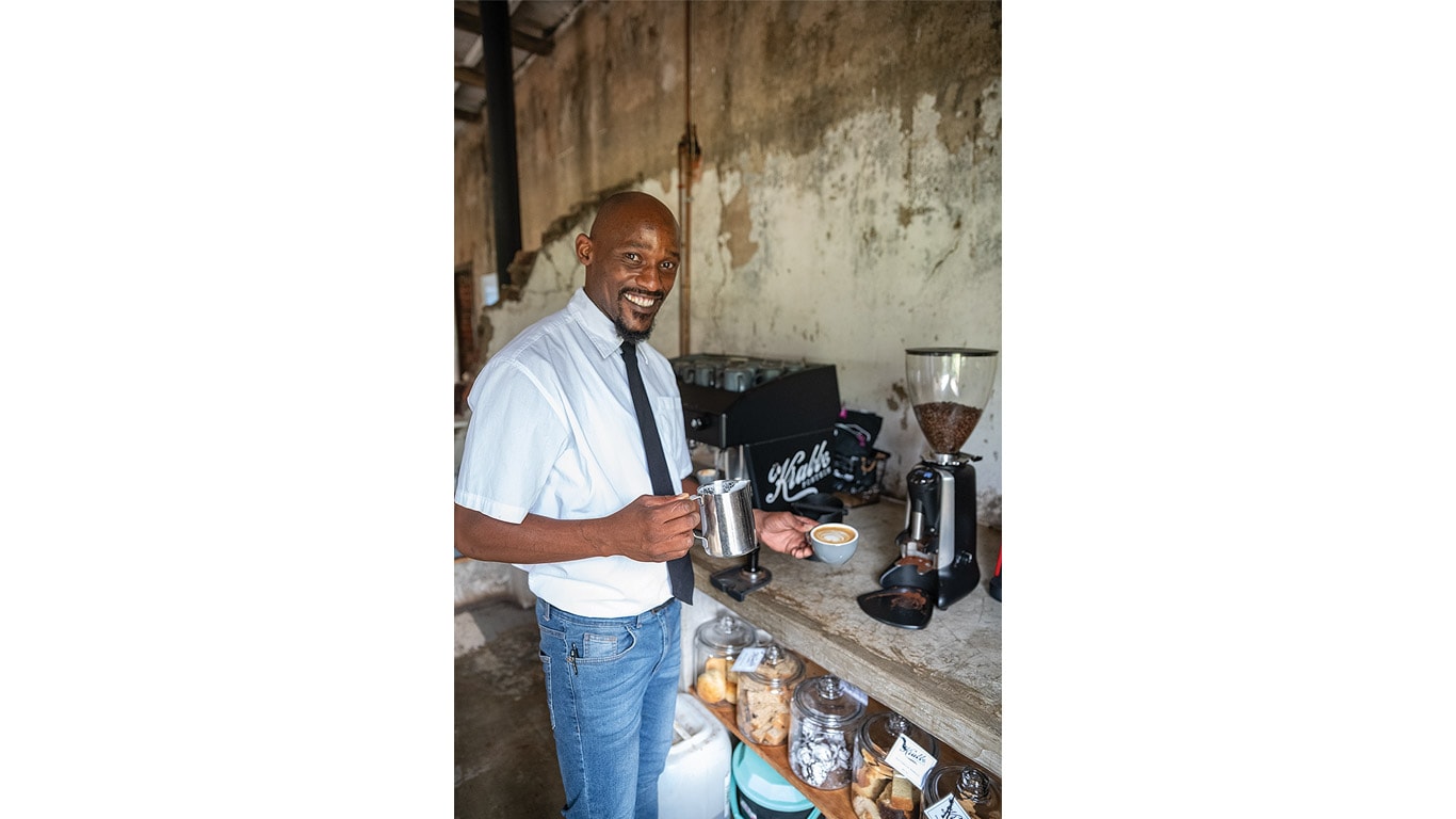 A person in white shirt and tie, holding a coffee pot and cup.