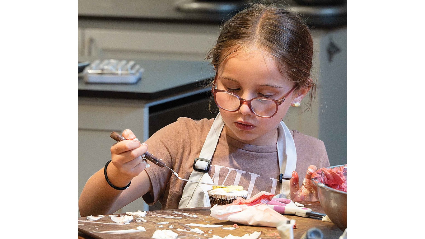 Child decorating a cupcake at a kitchen workstation.