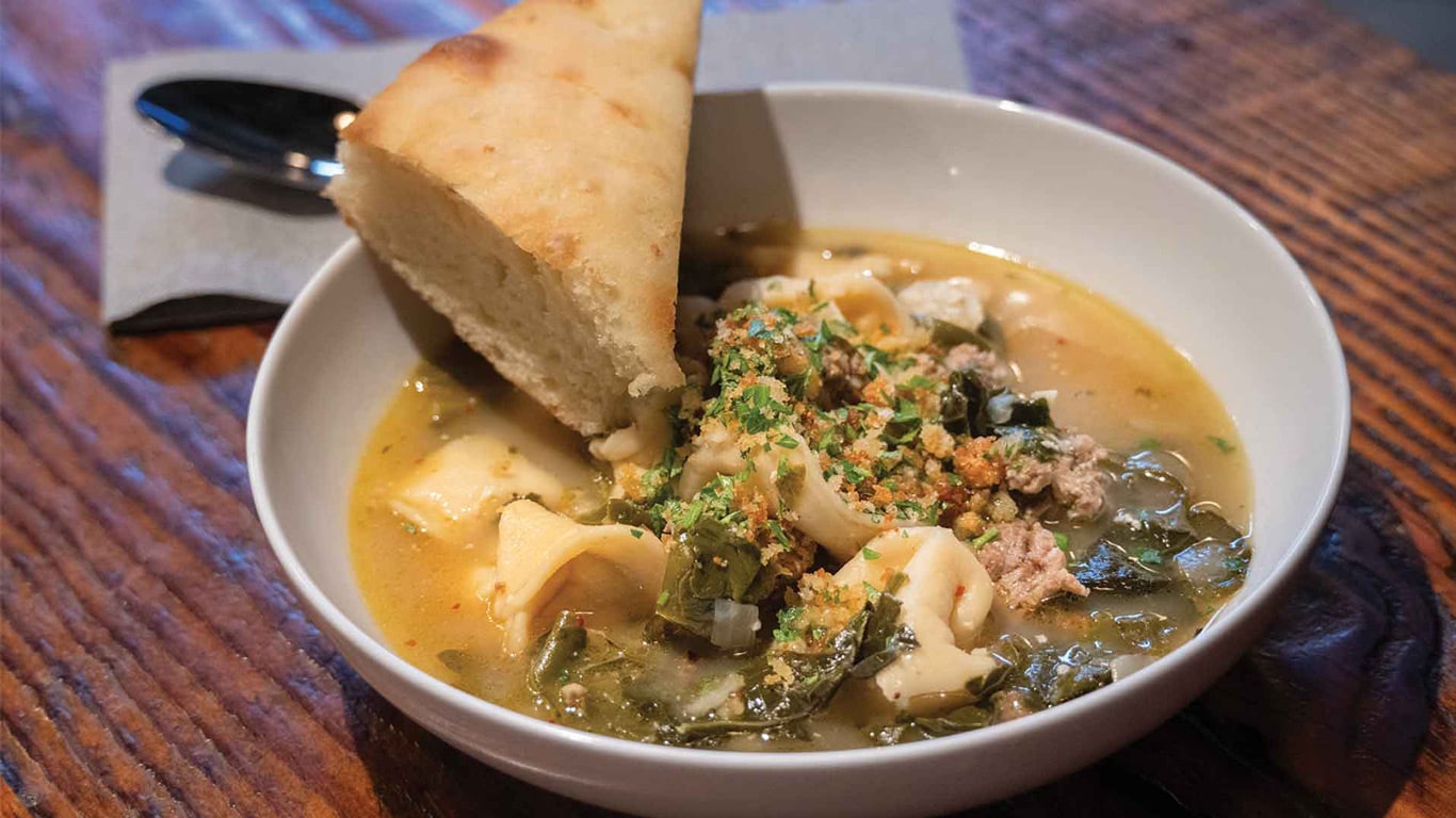 Bowl of soup with pasta, greens, and bread on the side.