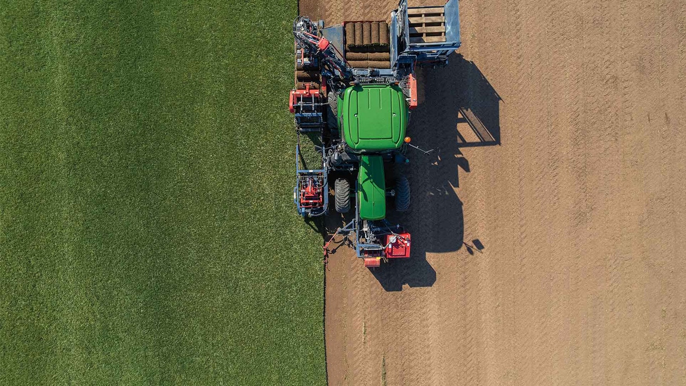 Top‑down view of a tractor operating on a field, between soil to grass.