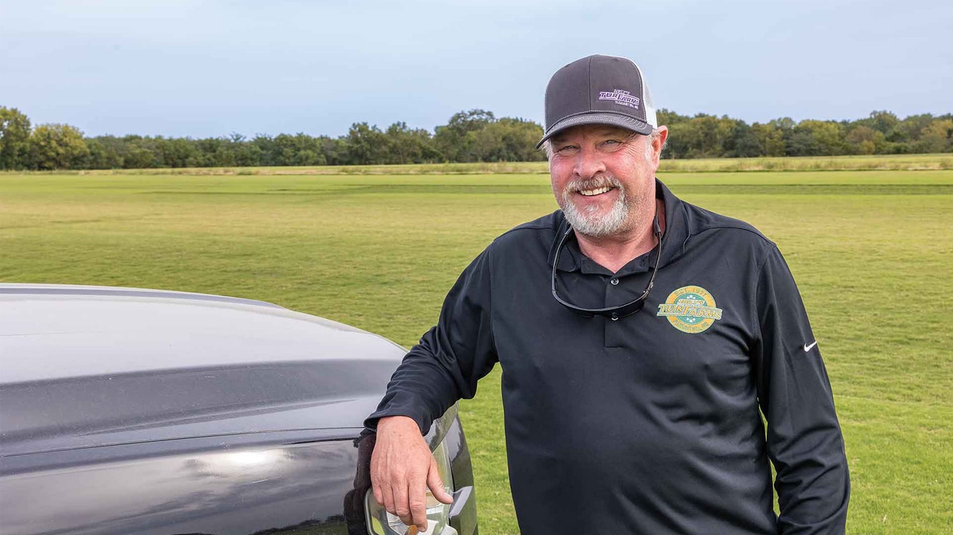 Person standing next to a vehicle on a large grassy field.