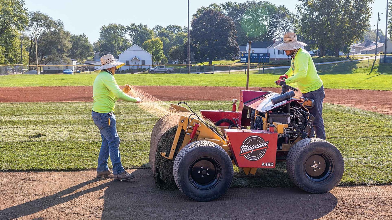 Workers installing sod using a turf‑laying machine on a sports field.