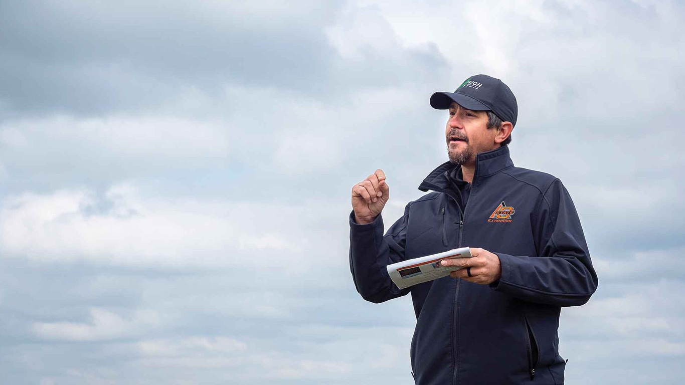 Person in outdoor workwear holding a notebook under a cloudy sky.
