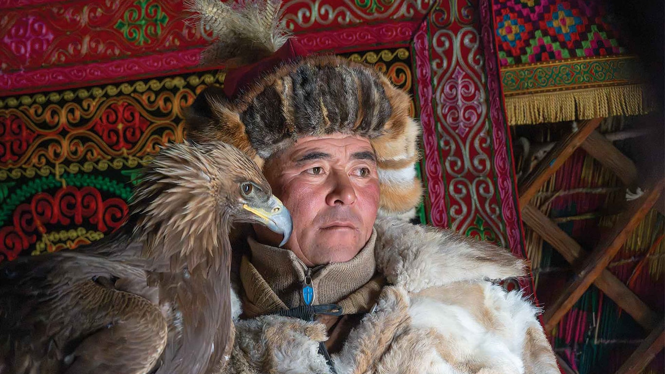 A person in fur clothing holding a golden eagle inside a decorated yurt.