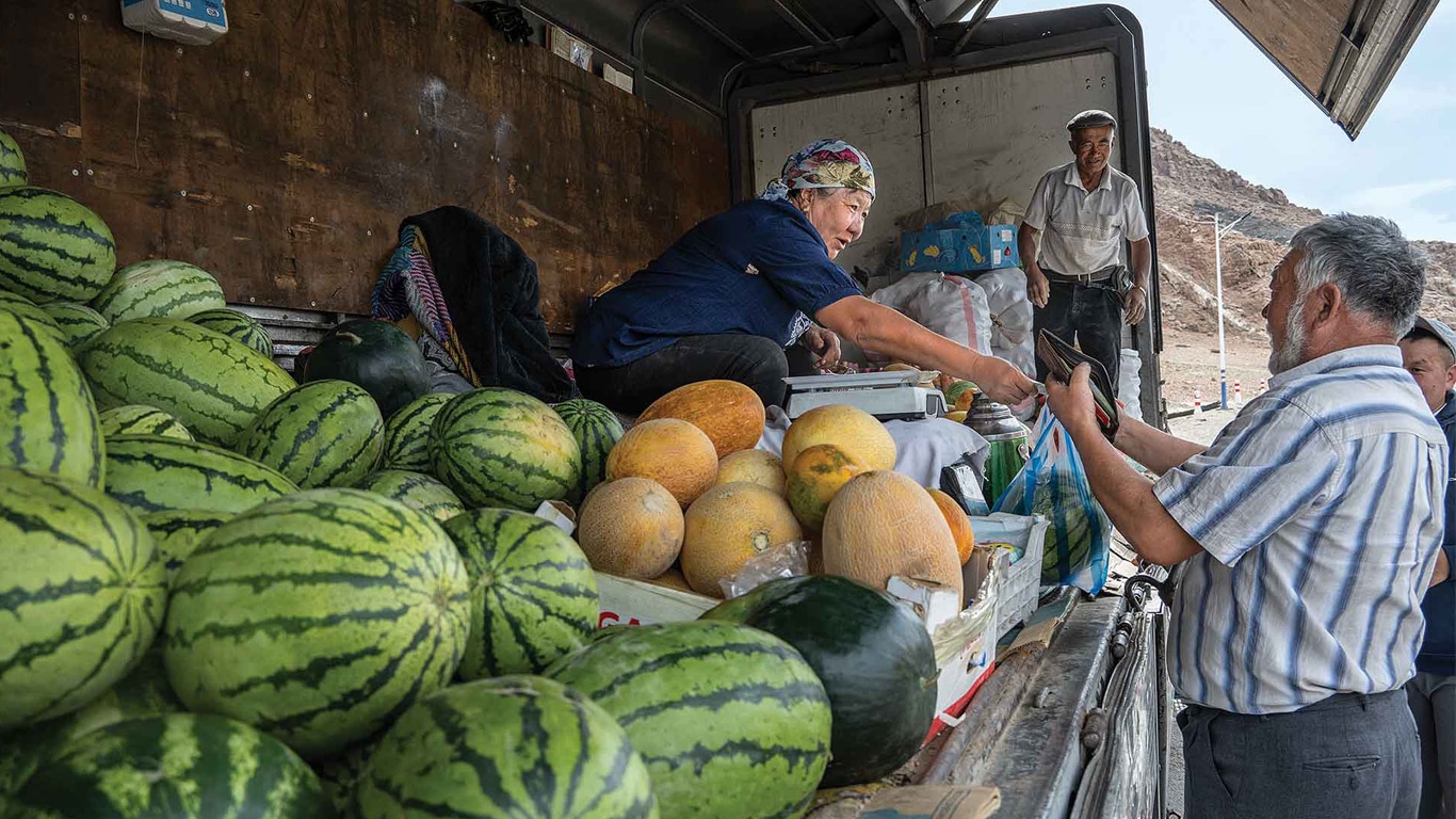 People buying and selling melons from the back of a truck.