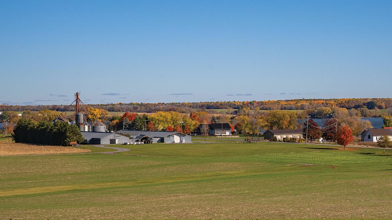 Rural farm with fields, barns, and silos amid fall-colored trees.