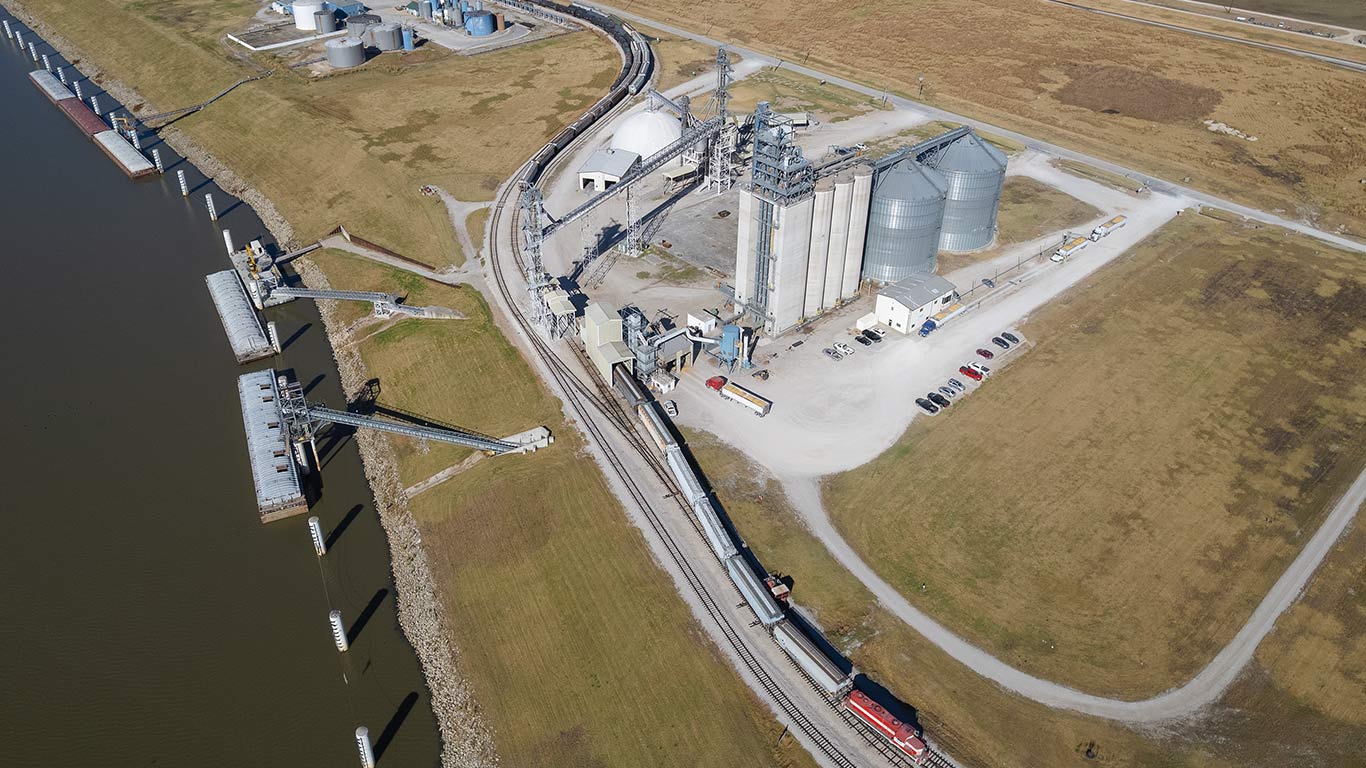 Vue aérienne d'une installation de manutention du grain comprenant des silos, des wagons et un quai de chargement de barge fluviale.