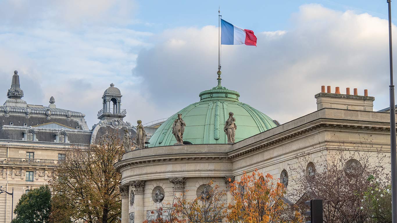 Historic building with a domed roof and a French flag flying above classical architectural details.