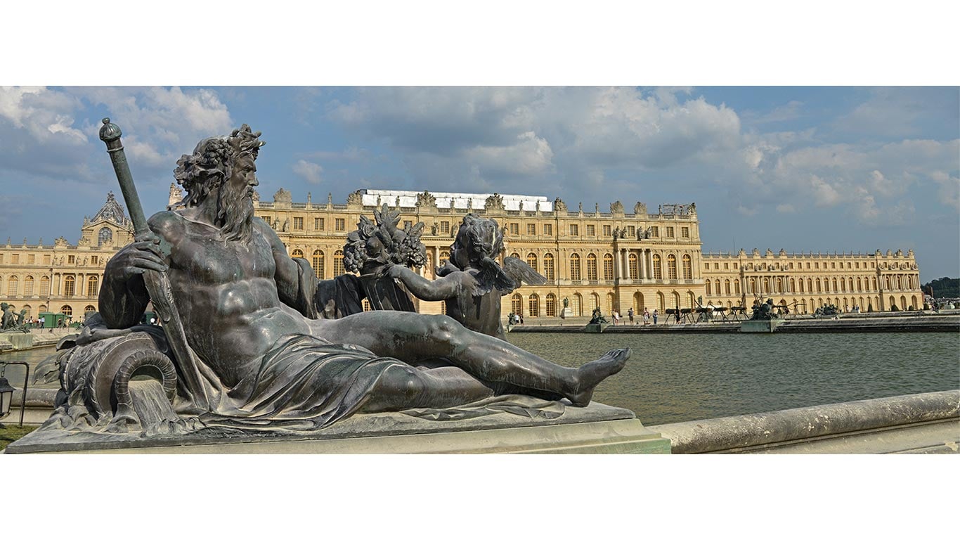 Classical statue beside a reflecting pool with a large historic palace in the background.