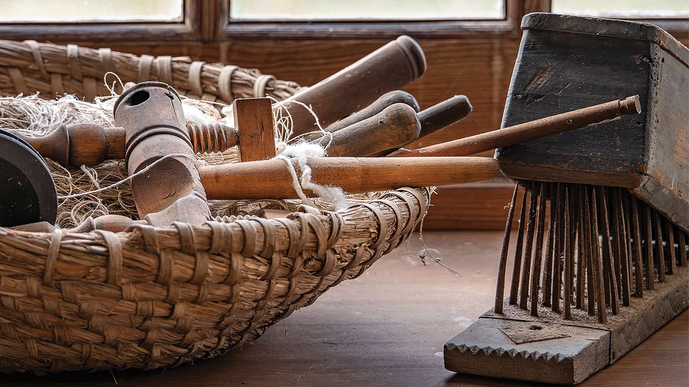 Basket of antique wooden tools next to a metal rake on a wooden surface.