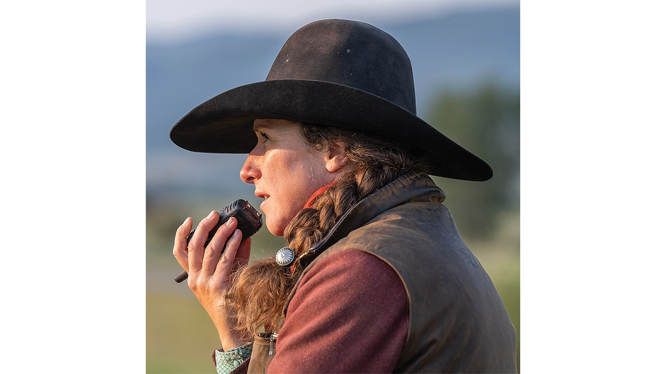 Une personne avec un chapeau de cow-boy qui parle dans un talkie-walkie avec le soleil dans le visage.
