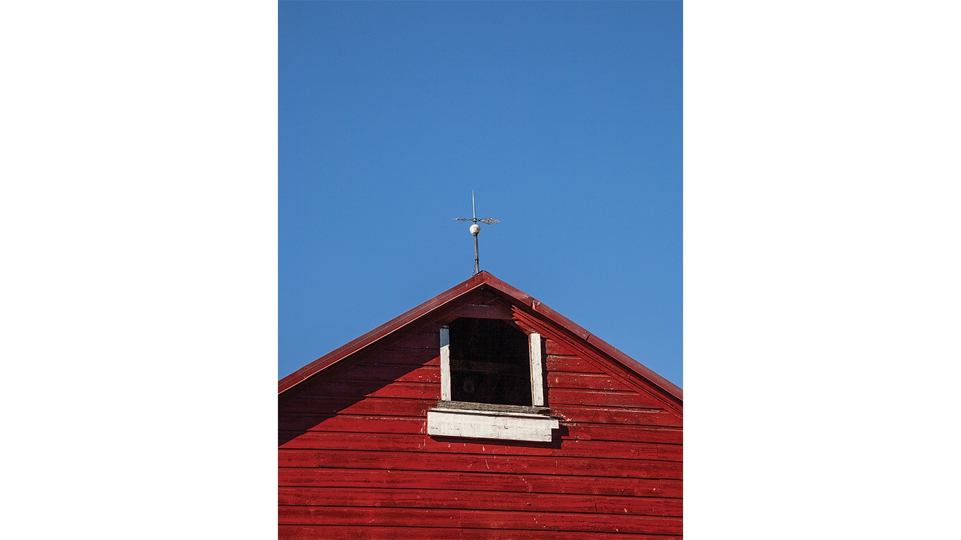 Upper section of a red wooden building with a small window and a weather vane on the roof.