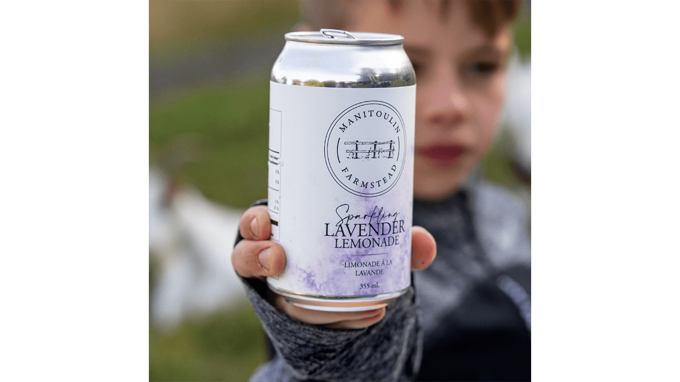 Enfant qui tient une canette de limonade p&eacute;tillante &agrave; la lavande avec le logo d'une ferme devant un arri&egrave;re-plan flou.