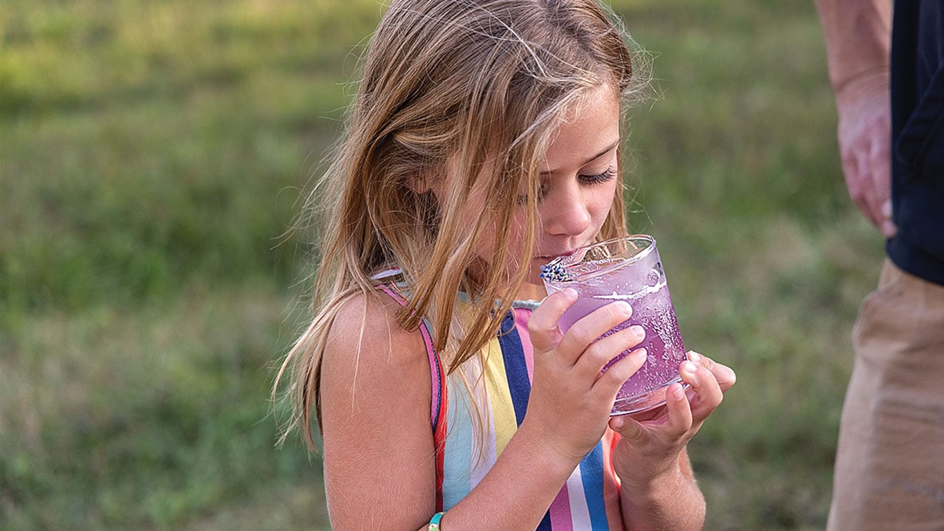 Enfant buvant une boisson violette dans un verre à l'extérieur.