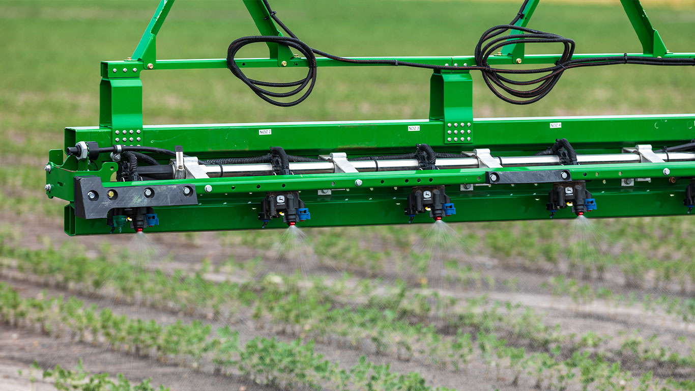 Photo d'un herbicide sortant d'une buse de pulvérisation d'un pulvérisateur automoteur travaillant dans le champ.