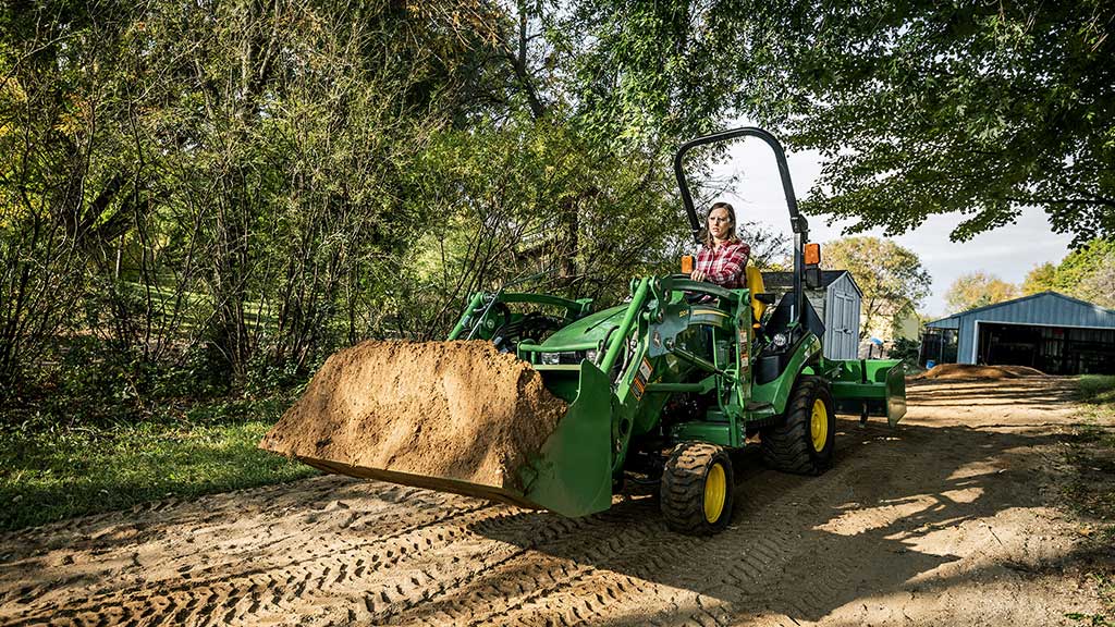 Femme au volant d'un tracteur utilitaire compact dont le chargeur est plein de terre