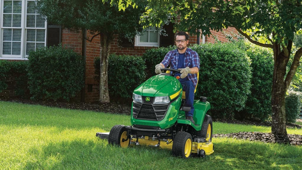 Homme tondant la pelouse de sa cour avant avec un tracteur de pelouse