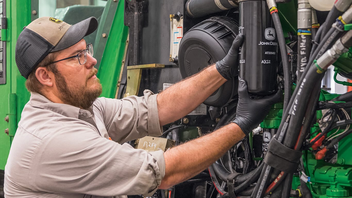 Un technicien effectue l’entretien d’une machine John Deere et remplace le filtre